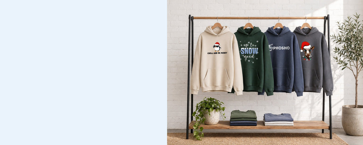 4 printed pullover hoodies on wooden hangers on a wood and iron clothing rack against a sunlit white brick wall, with an olive tree, trailing pothos and folded tees on the shelf below