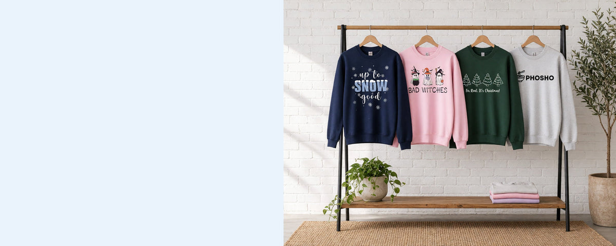 4 printed crewneck sweatshirts on wooden hangers on a wood and iron clothing rack against a sunlit white brick wall, with an olive tree, trailing pothos and folded tees on the shelf below