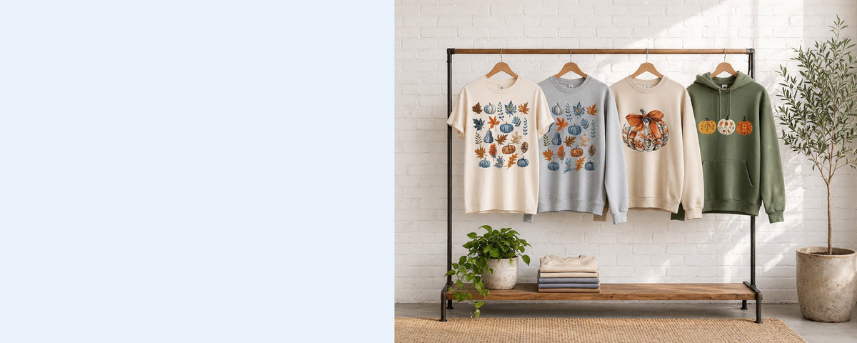 4 printed garments on wooden hangers on a wood and iron clothing rack against a sunlit white brick wall, with an olive tree, trailing pothos and folded tees on the shelf below