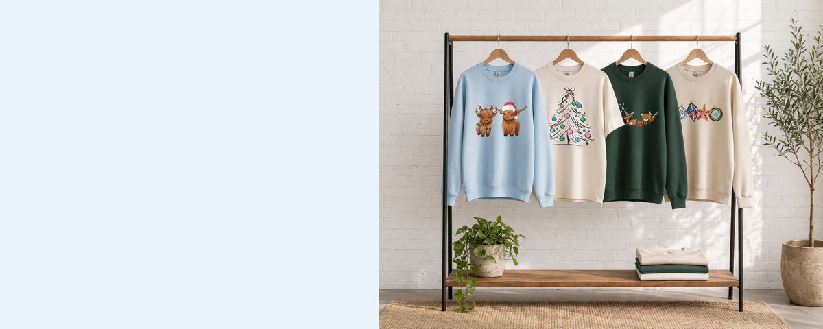 4 printed garments on wooden hangers on a wood and iron clothing rack against a sunlit white brick wall, with an olive tree, trailing pothos and folded tees on the shelf below