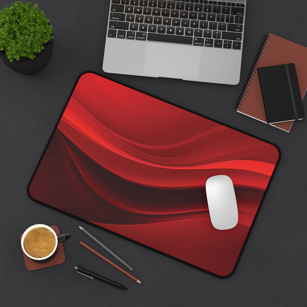 Abstract Red Wave Desk Mat from above on a desk with laptop, plant, notebooks, coffee cup, pens and mouse, 12 × 18 inches.