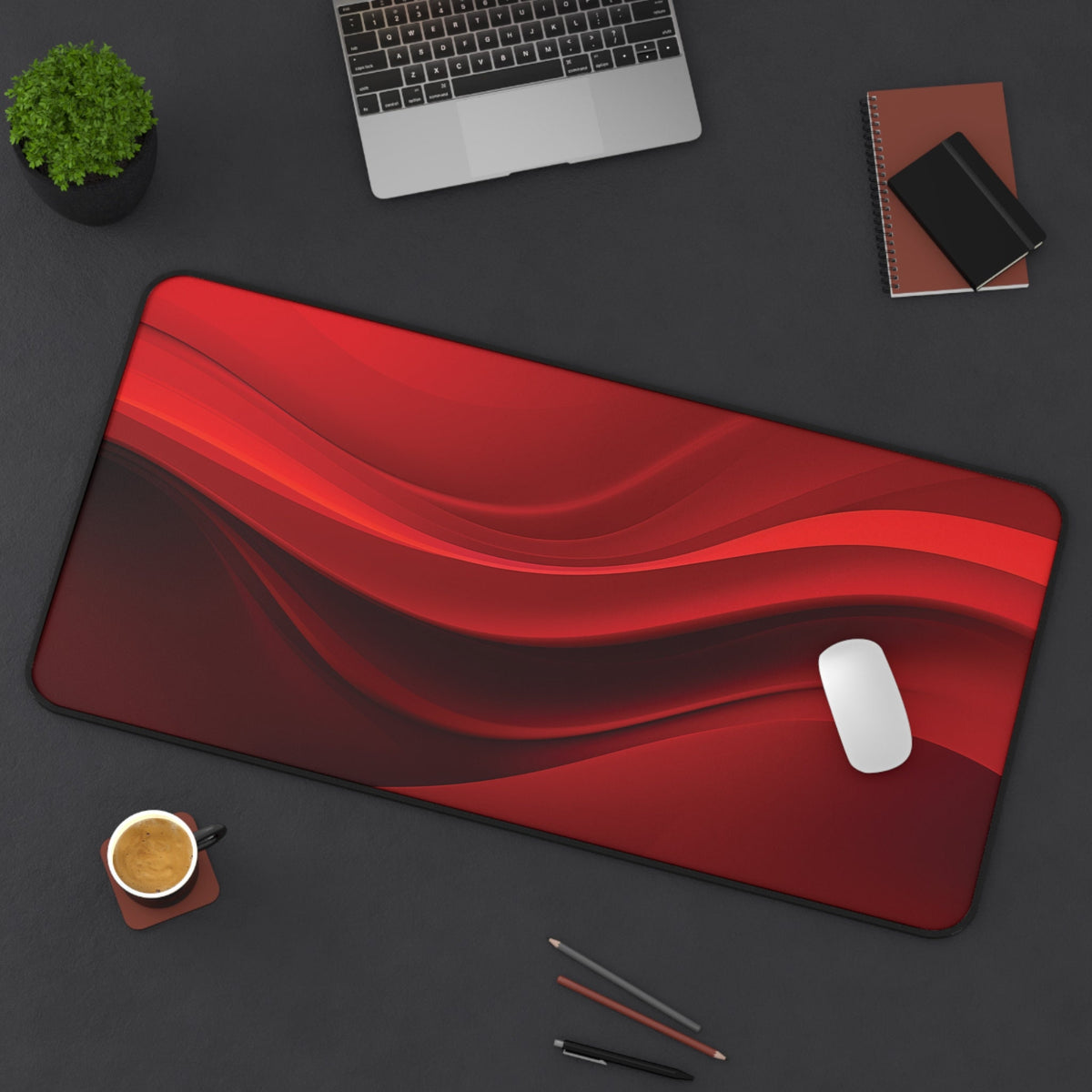 Abstract Red Wave Desk Mat, 16 × 32 inches, on a dark desk from above with a laptop, plant, coffee, notebooks and pens.
