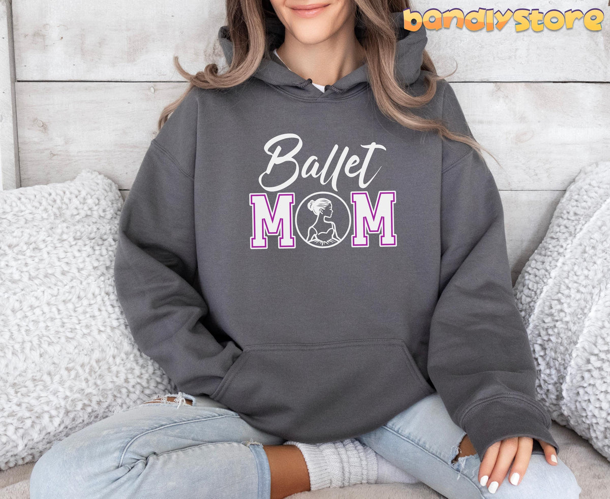 Ballet Mom Hoodie in charcoal, front view on woman seated cross-legged by white pillows against wood wall.