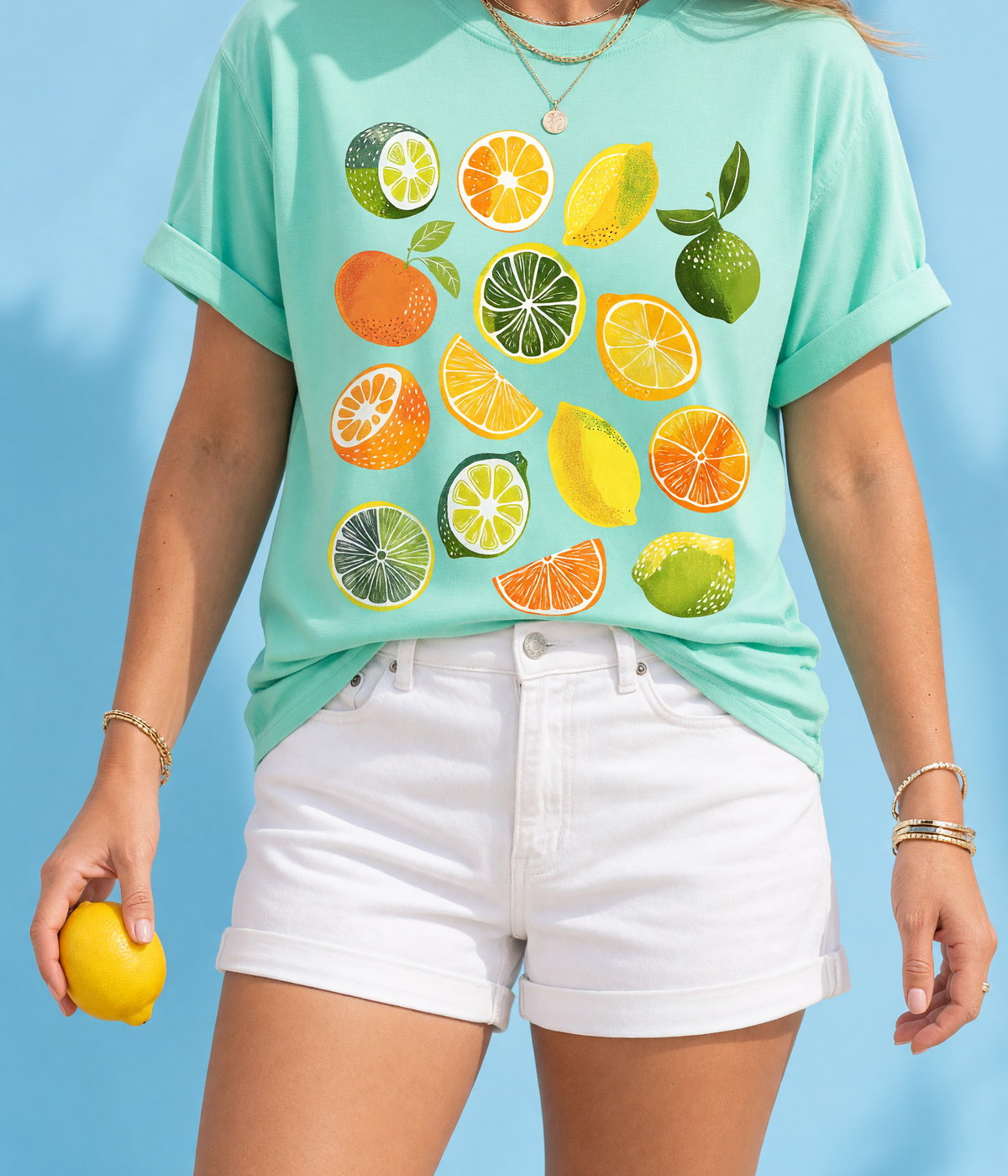 A woman in a printed citrus t-shirt holding a lemon, cropped at the shoulders, against a sky-blue backdrop