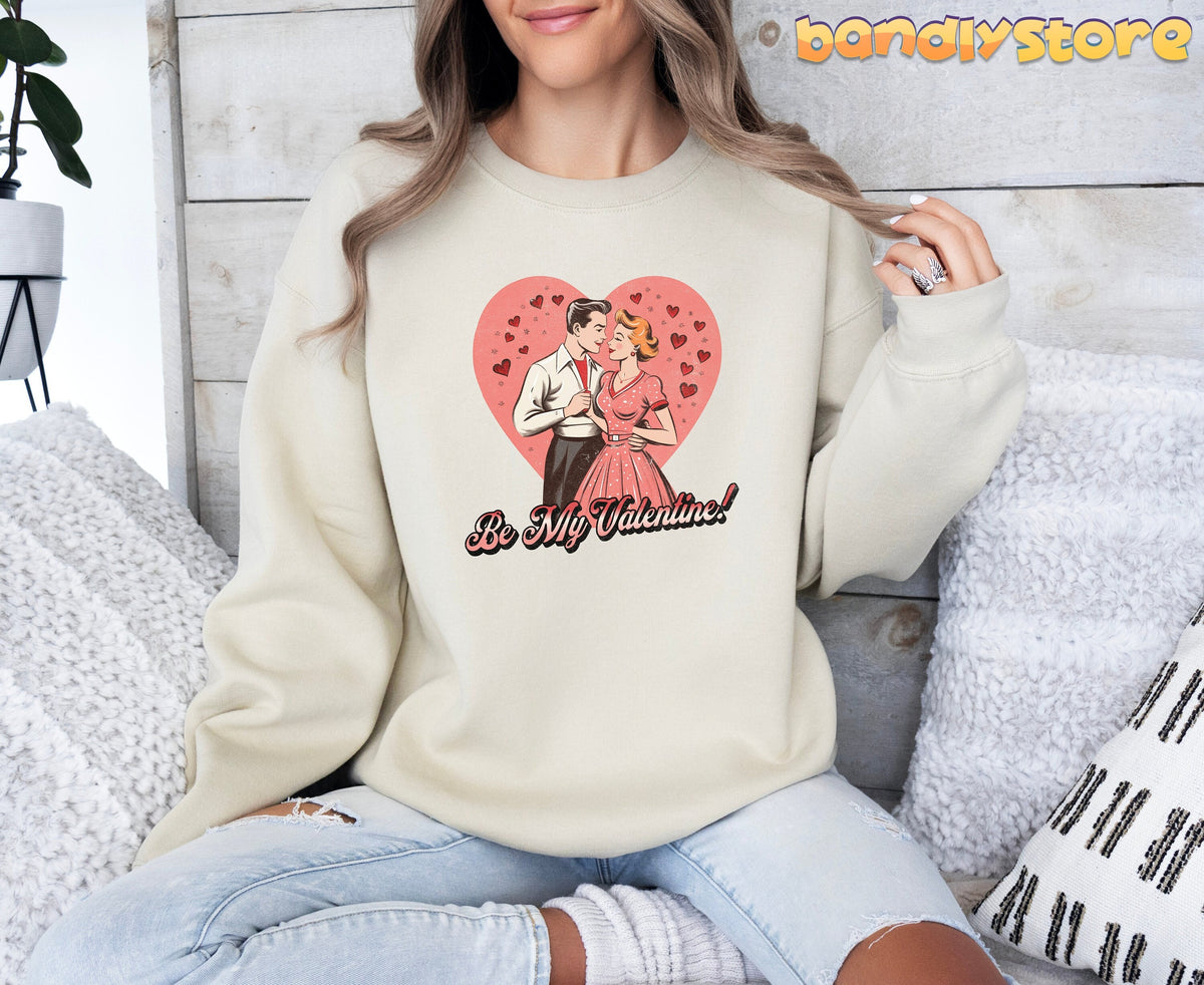 Be Mine Valentine Sweatshirt in sand on a woman seated amid pillows against a wooden wall.