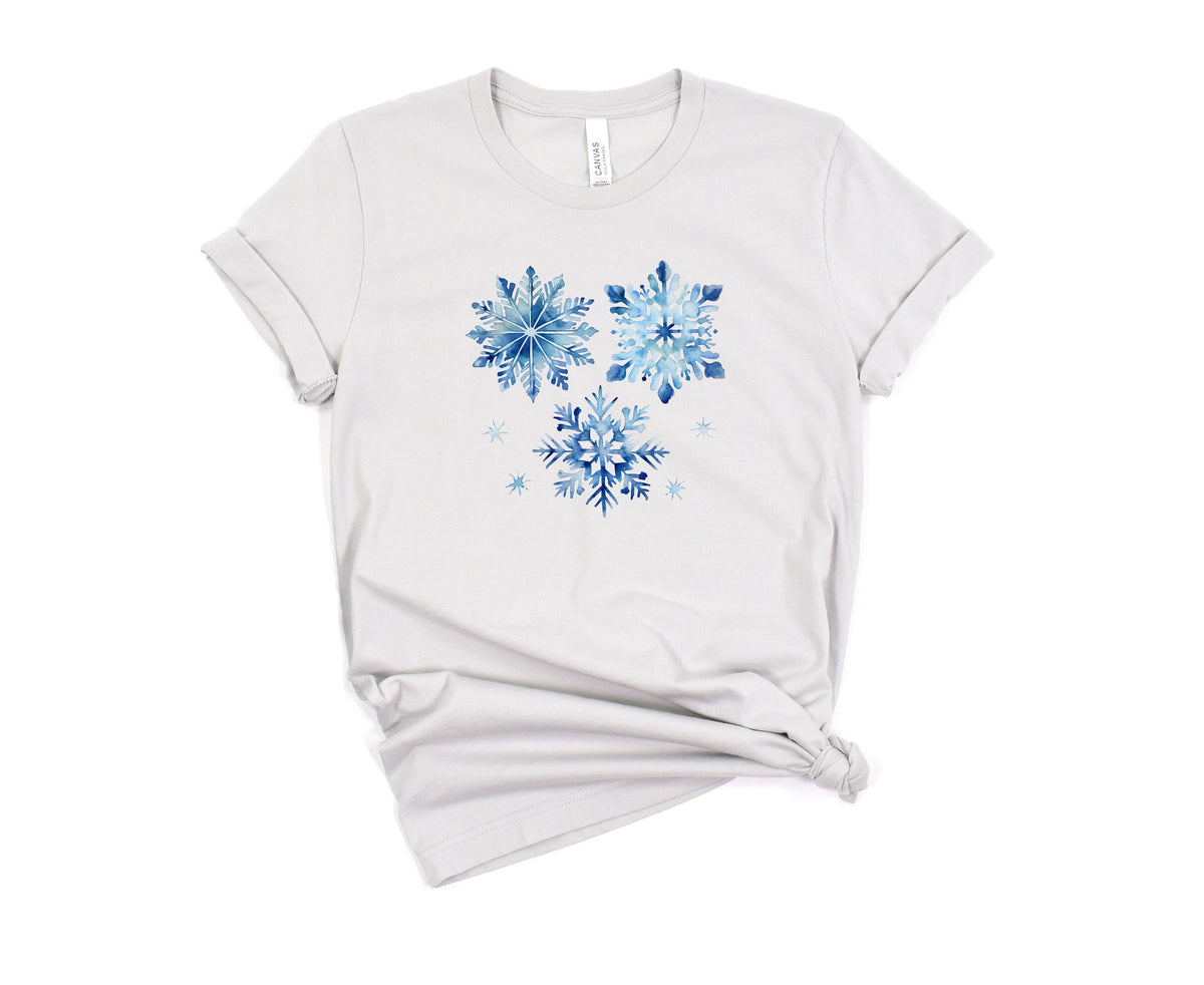 Watercolor Snowflakes T-Shirt in silver laid flat on a white background with rolled sleeves and knotted hem.