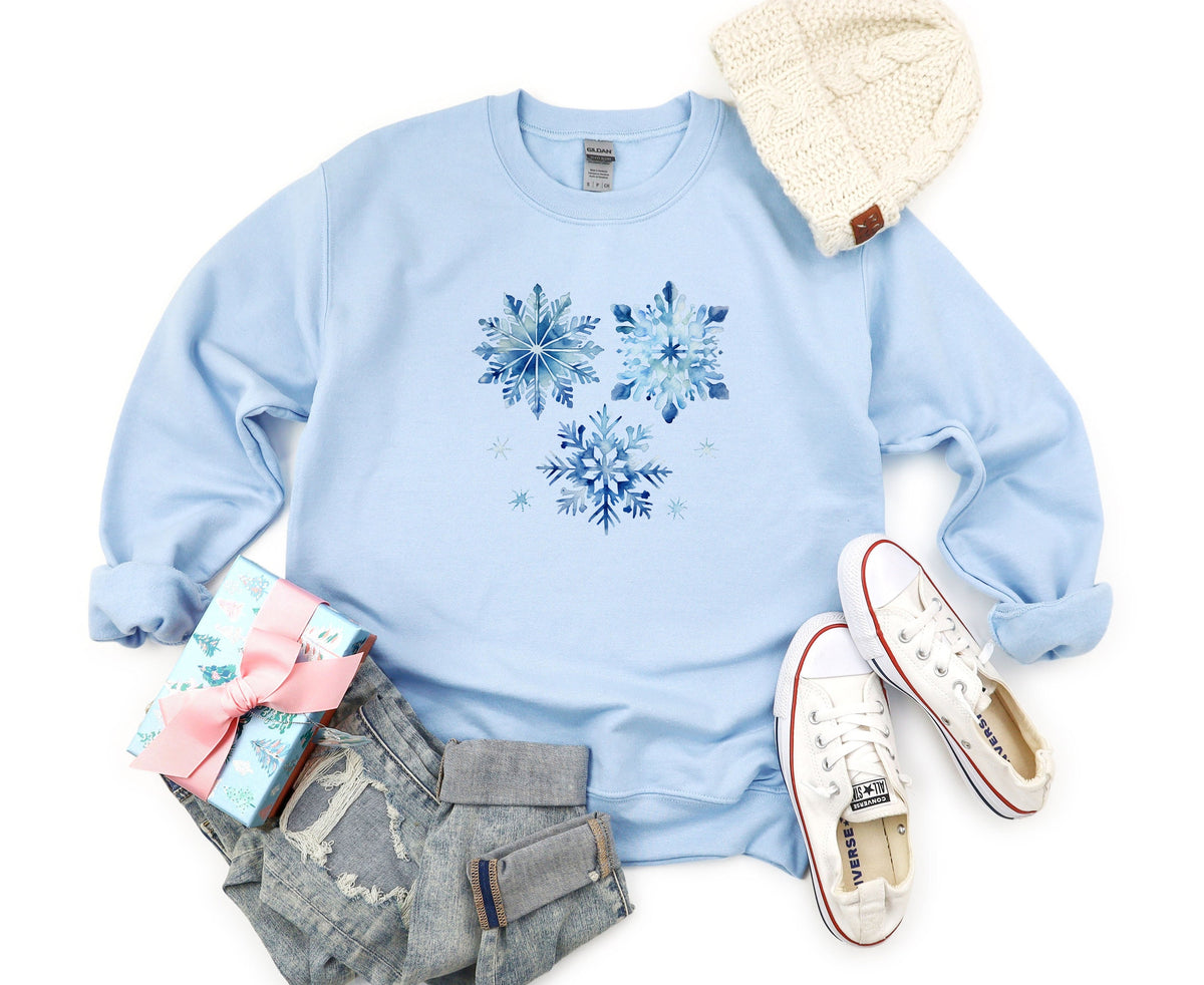 Blue Watercolor Snowflakes Sweatshirt in light blue, flat lay with beanie, gift, jeans and sneakers.