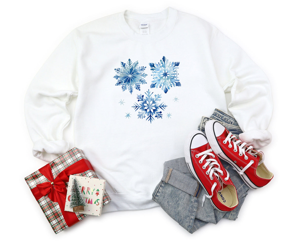 Blue Watercolor Snowflakes Sweatshirt in white laid flat beside gifts, jeans and red sneakers.