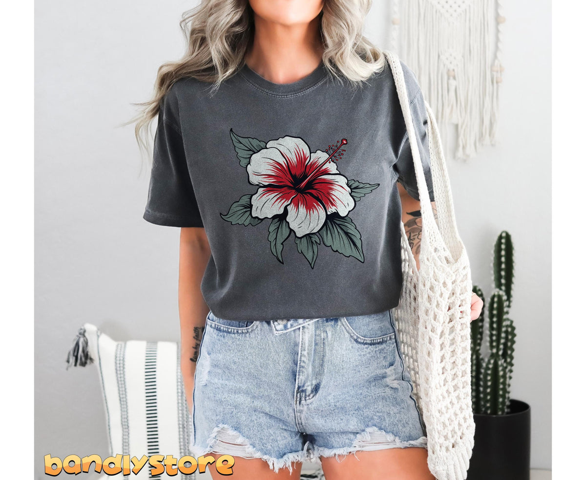 Boho Hibiscus Flower T-Shirt in pepper on a model facing camera in denim shorts holding a woven bag next to a cactus.