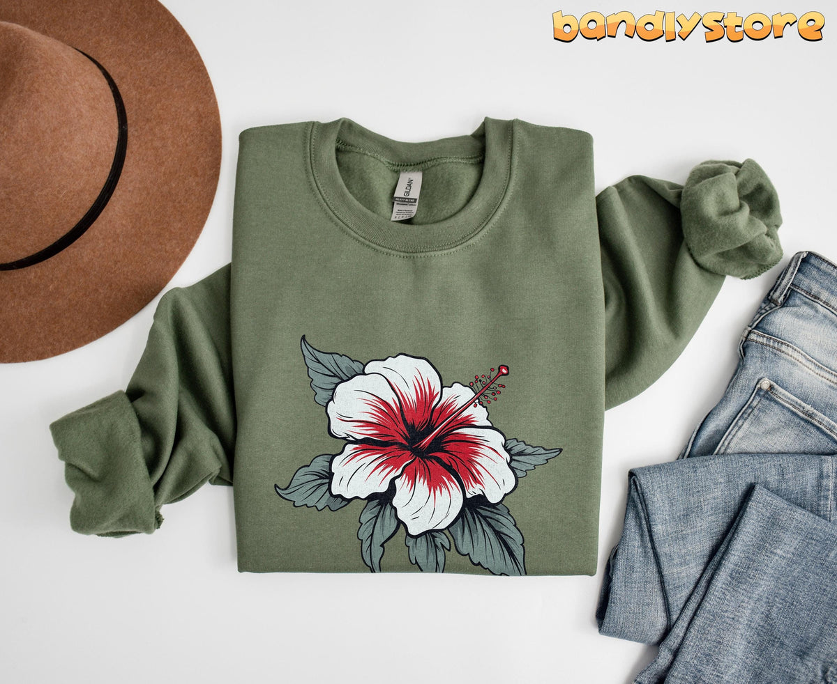 Boho Hibiscus Sweatshirt in military green, folded flat beside a brown hat and blue jeans.