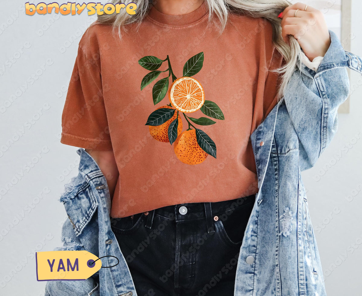 Boho Oranges T-Shirt in yam on a person with blonde hair holding a denim jacket, front view, plain wall.
