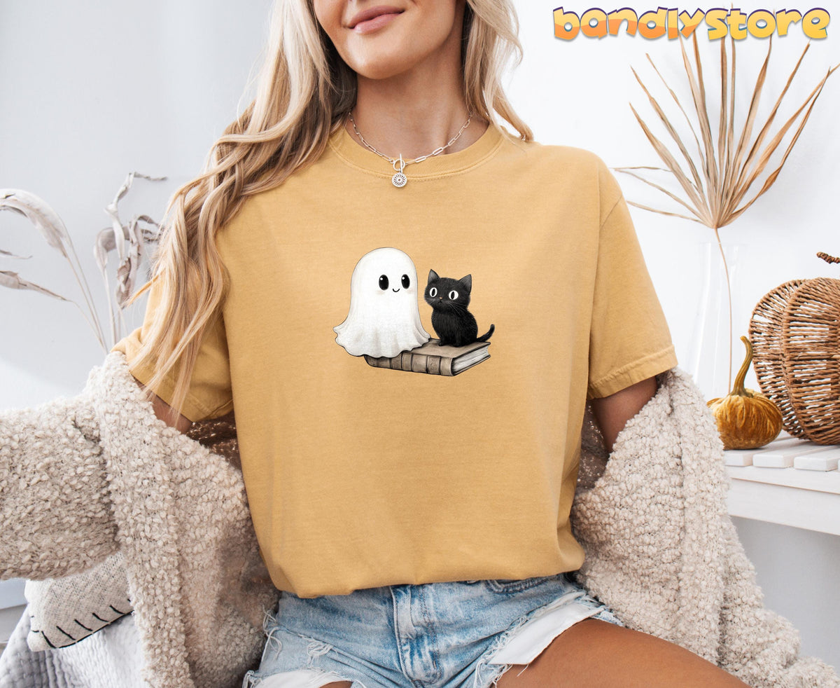Cute Bookish Ghost T-Shirt in mustard on a seated model amid dried plants and woven pumpkins.