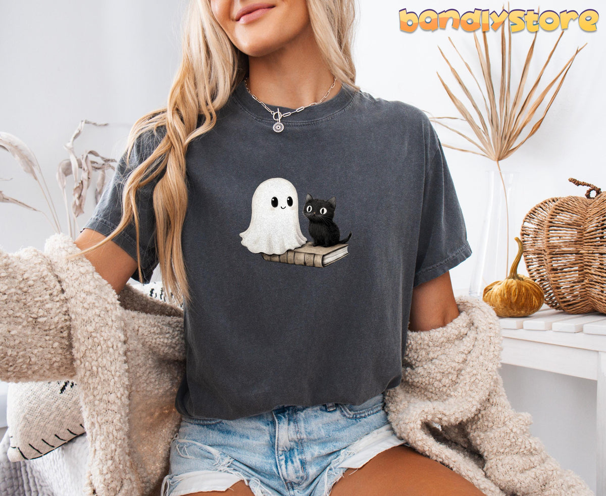 Cute Bookish Ghost T-Shirt in Pepper on a seated model amid dried plants, a pumpkin and woven baskets.
