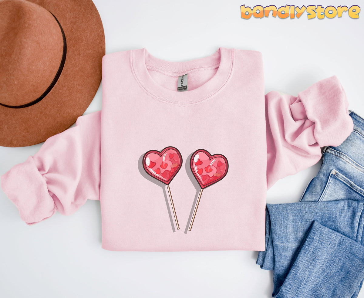 Cute Candy Hearts Sweatshirt in light pink laid flat from above beside a brown hat and blue jeans.