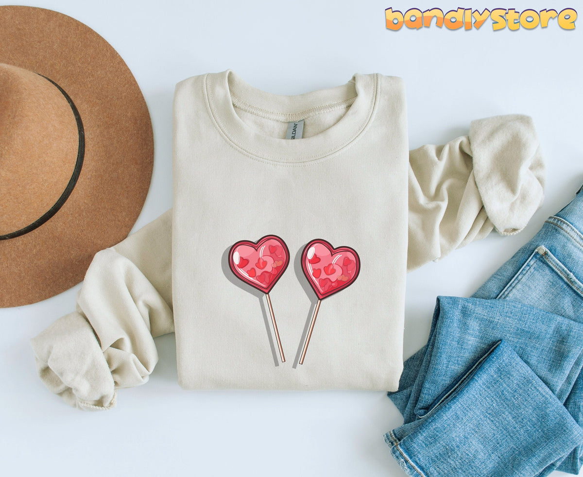 Cute Candy Hearts Sweatshirt in sand, flat-laid from above beside a brown hat and blue jeans.
