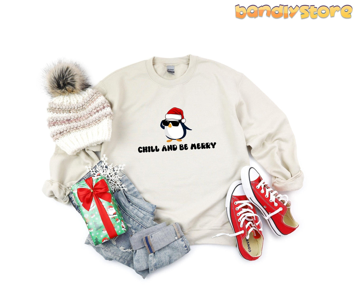 Chill And Be Merry Penguin Sweatshirt in sand, flat-lay with beanie, jeans, gift and red sneakers.