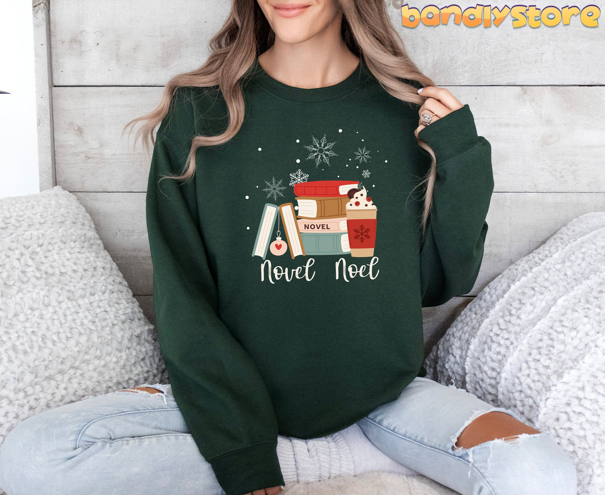 Novel Noel Christmas Sweatshirt in forest green on a person seated amid white pillows against a wood-paneled wall.