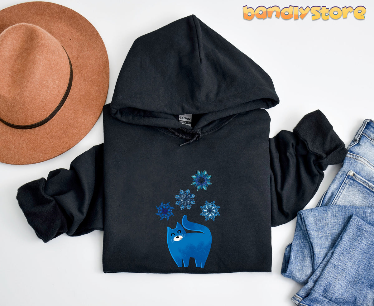 Christmas Cat And Snowflakes Hoodie in black, flat-lay with brown hat left and blue jeans right.