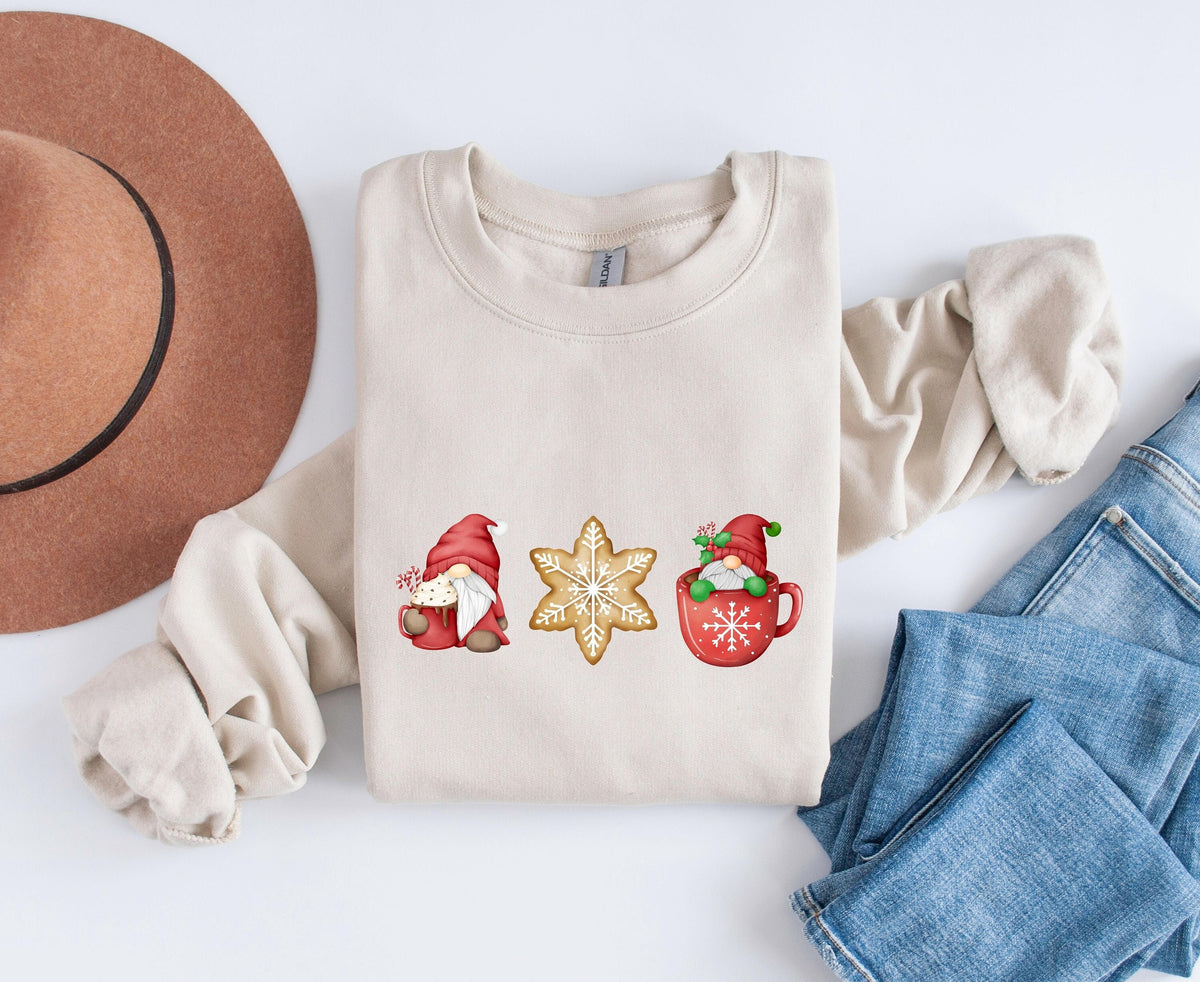 Christmas Gnomes Gingerbread Sweatshirt in sand, folded flat beside a brown hat and blue jeans on white.