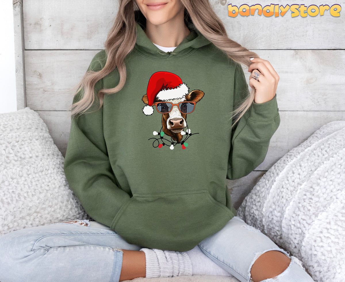 Christmas Highland Cow Hoodie in military green on a seated person against a light wood wall with white fluffy throws.