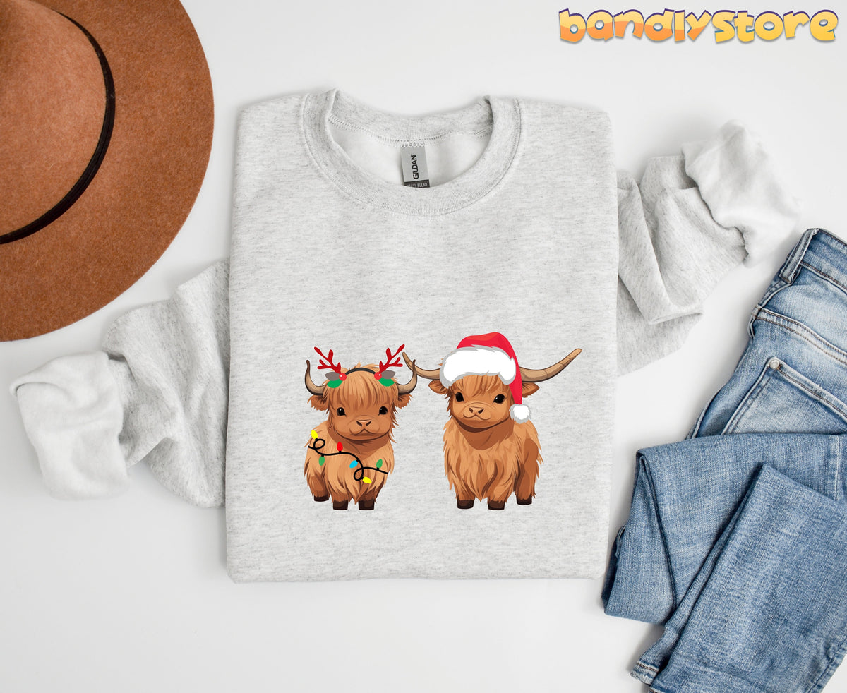 Christmas Highland Cow Sweatshirt in ash, flat-laid with brown hat left, folded jeans right, two festive cows centered.
