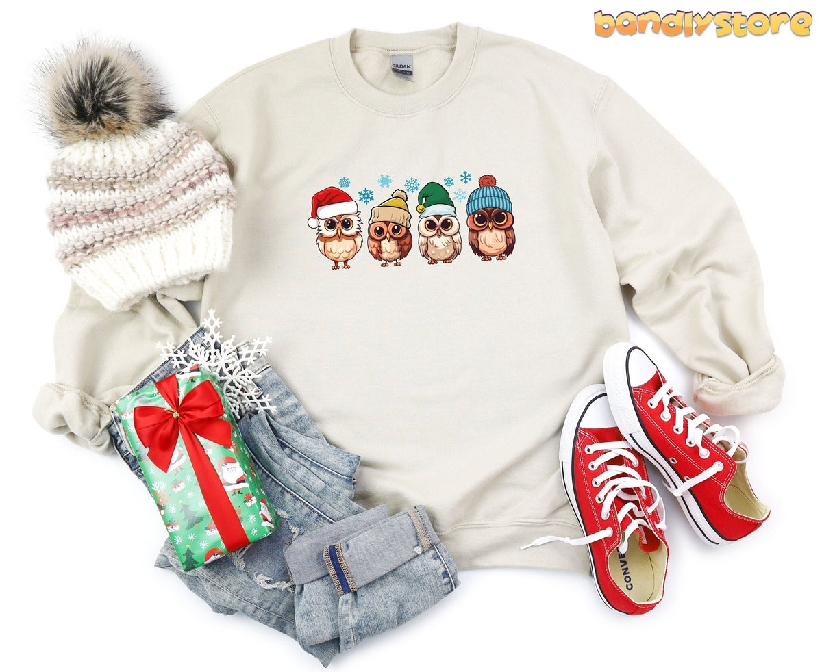 Cute Christmas Owl Sweatshirt in sand laid flat beside knit beanie, gift, jeans and sneakers.