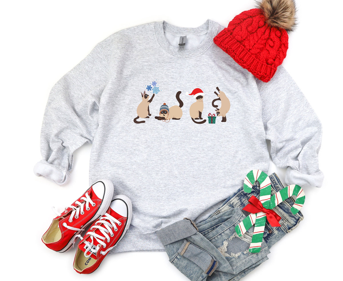 Christmas Siamese Cat Sweatshirt in ash, laid flat with a red beanie, red sneakers, jeans and candy canes nearby.