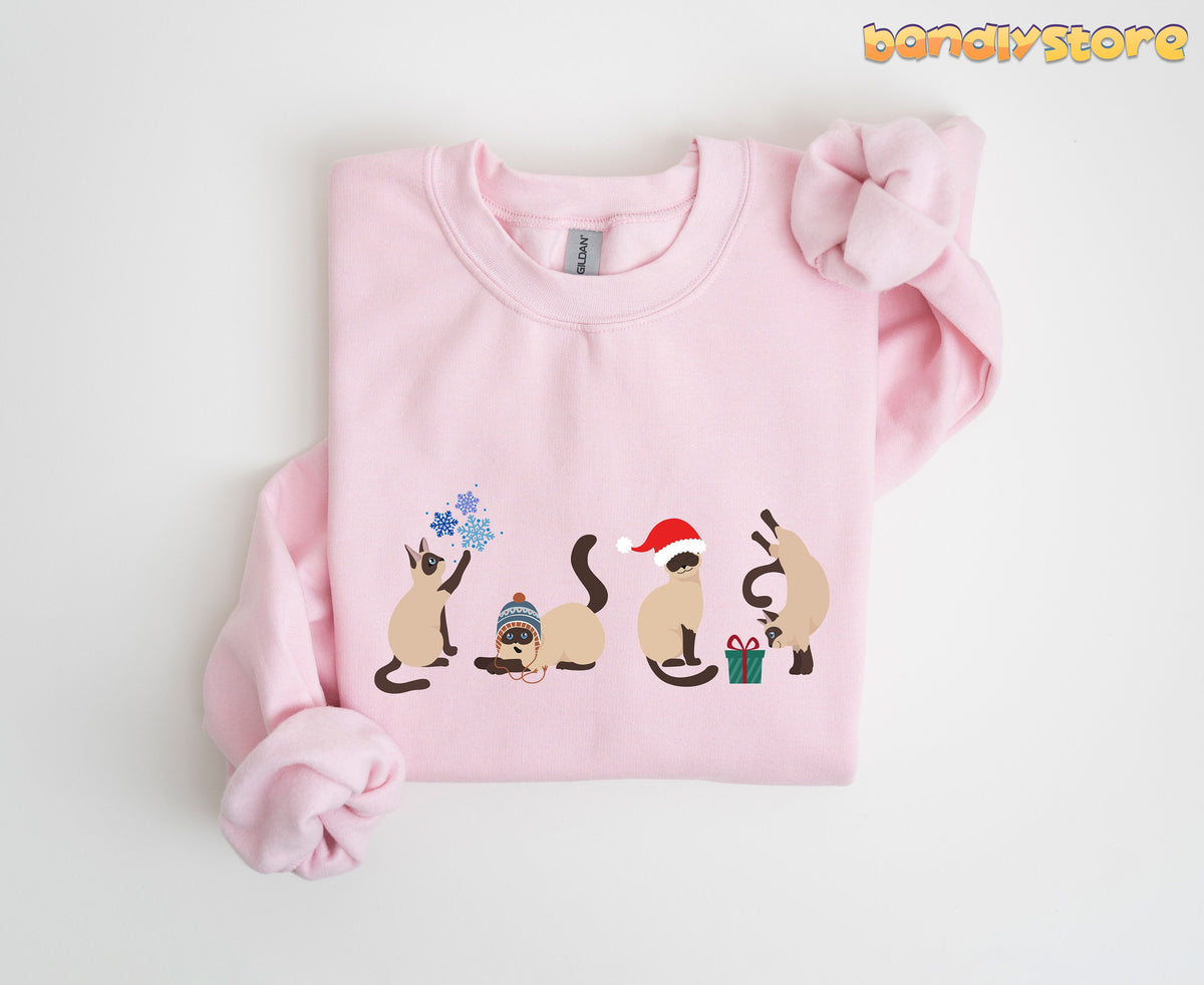 Christmas Siamese Cat Sweatshirt on light pink fabric, folded flat, four festive cats with snowflakes and gift.