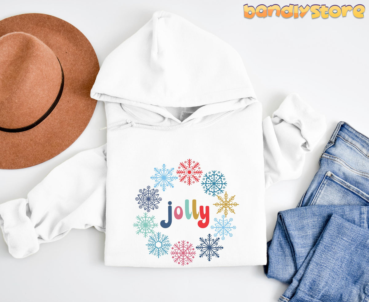 Christmas Snowflake Jolly Hoodie in white laid flat beside a brown hat and blue jeans.