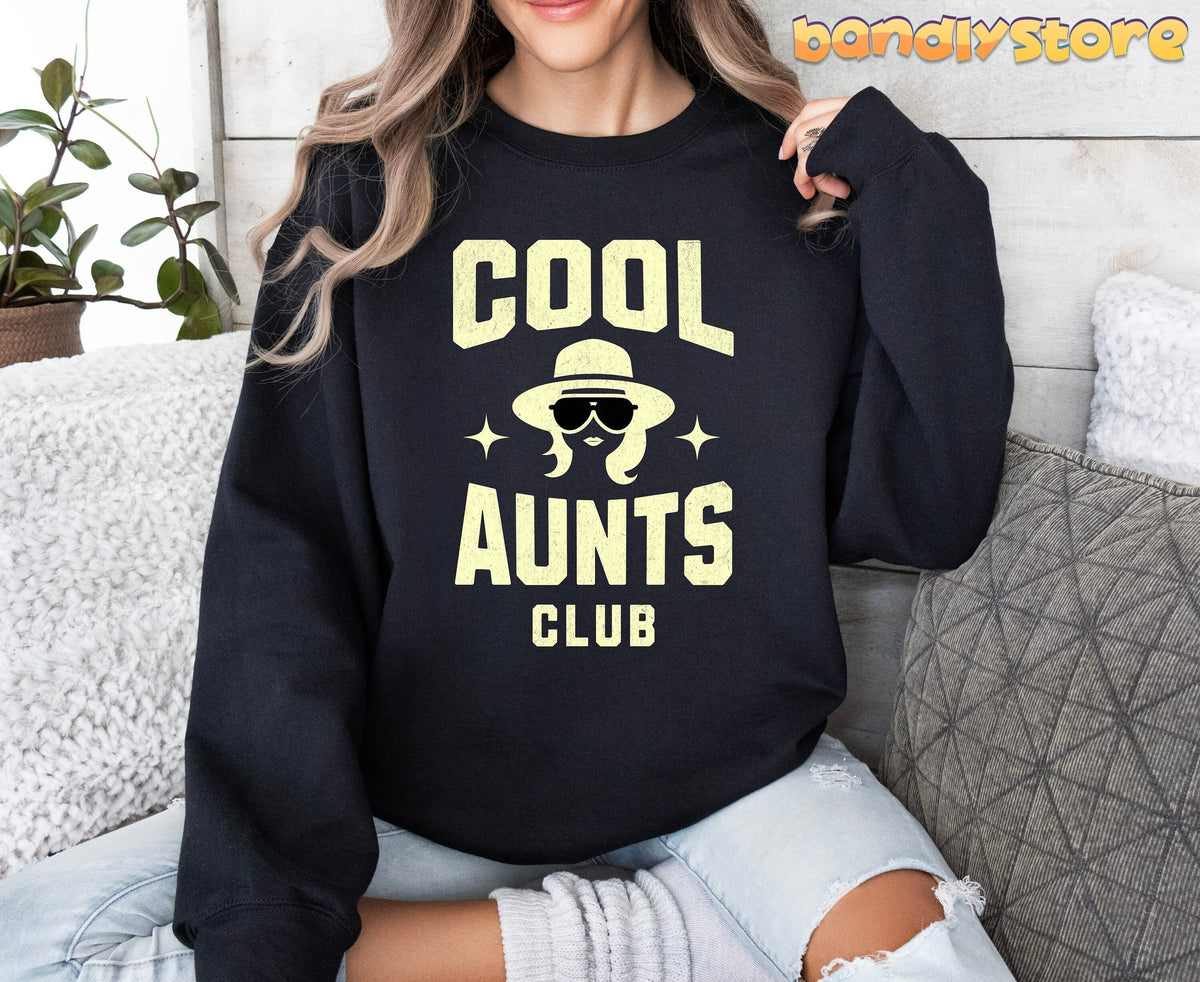 Cool Aunts Club Sweatshirt in black on a person seated front-facing on a couch with pillows and plant.