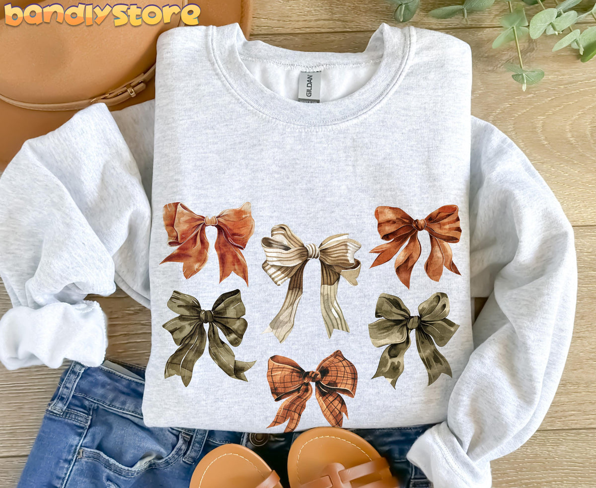 Fall Coquette Bow Sweatshirt in Ash, flat-lay on wood with hat, jeans, sandals and greenery beside it.