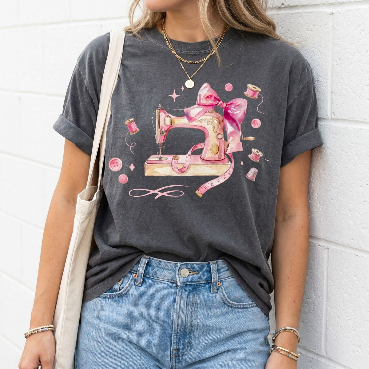 Coquette Sewing T-Shirt in pepper on a model against a white brick wall with tote bag and jeans.