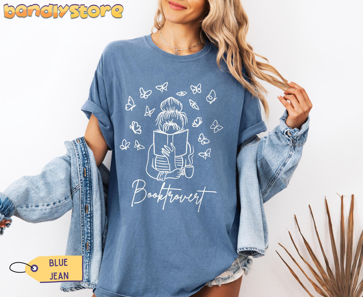 Booktrovert T-Shirt in Blue Jean on a model facing front with denim jacket over shoulders and plant at side.
