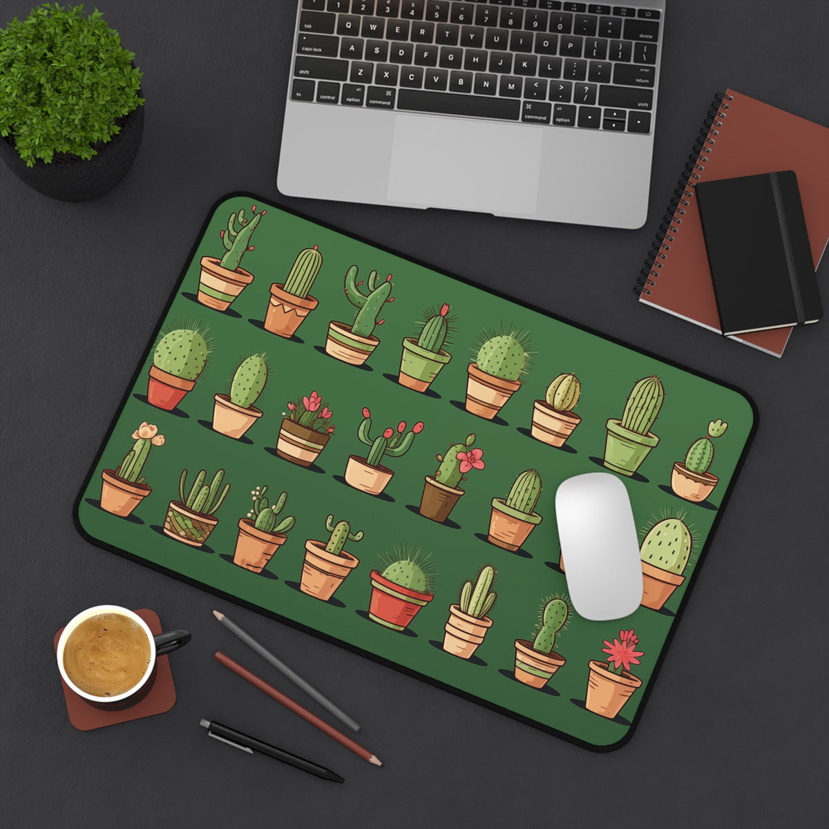 Cute Cacti Desk Mat 12 × 18 inches viewed from above on a dark desk with laptop, plant, notebooks, coffee, pens and mouse.