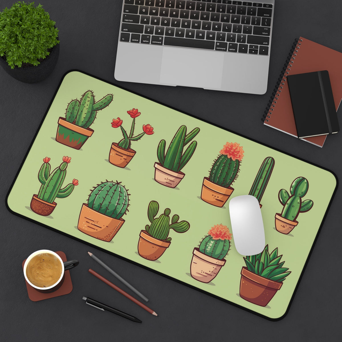 Cute Cactus Desk Mat from overhead on a dark desk next to a laptop, mouse, coffee cup, pencils and notebooks, 12 × 22 inches.