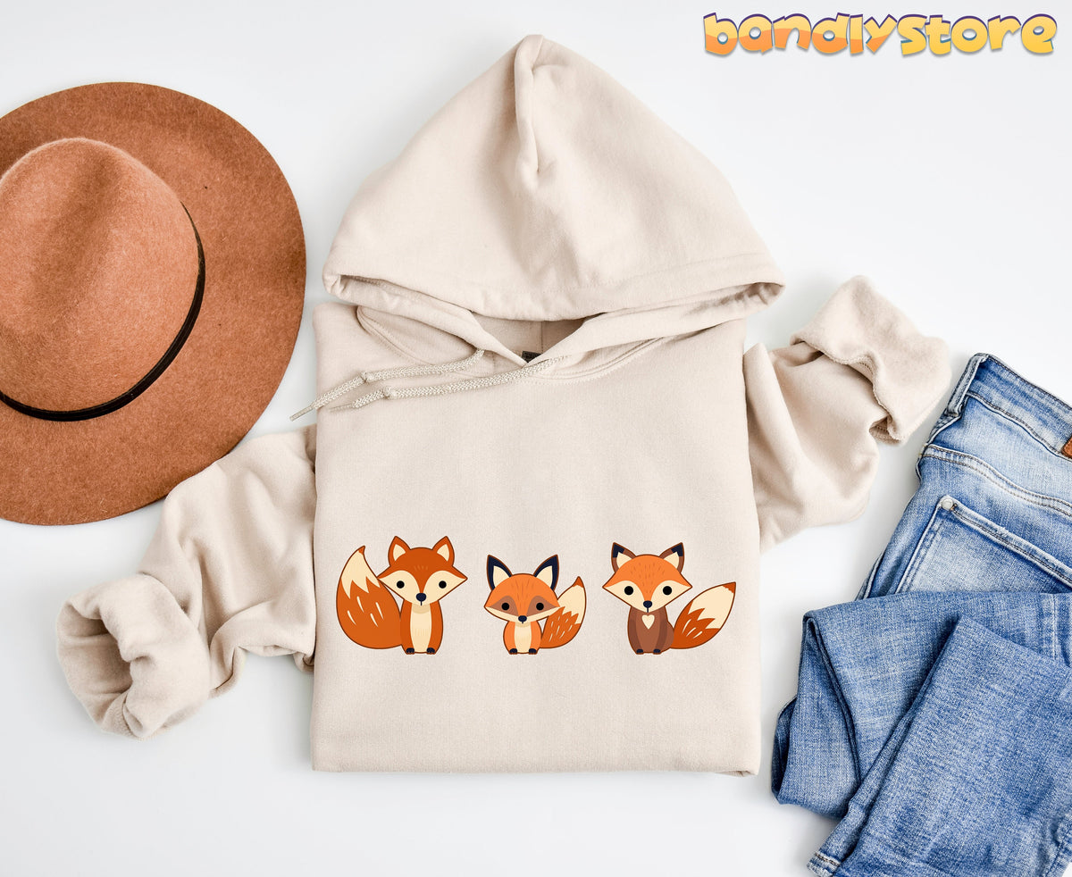 Cute Foxes Hoodie in sand flat-laid from above beside a brown hat and blue jeans.