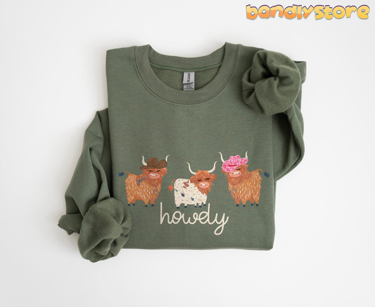 Cute Highland Cows Sweatshirt folded flat on white, sage green with three hat-wearing cows and howdy text in Military Green