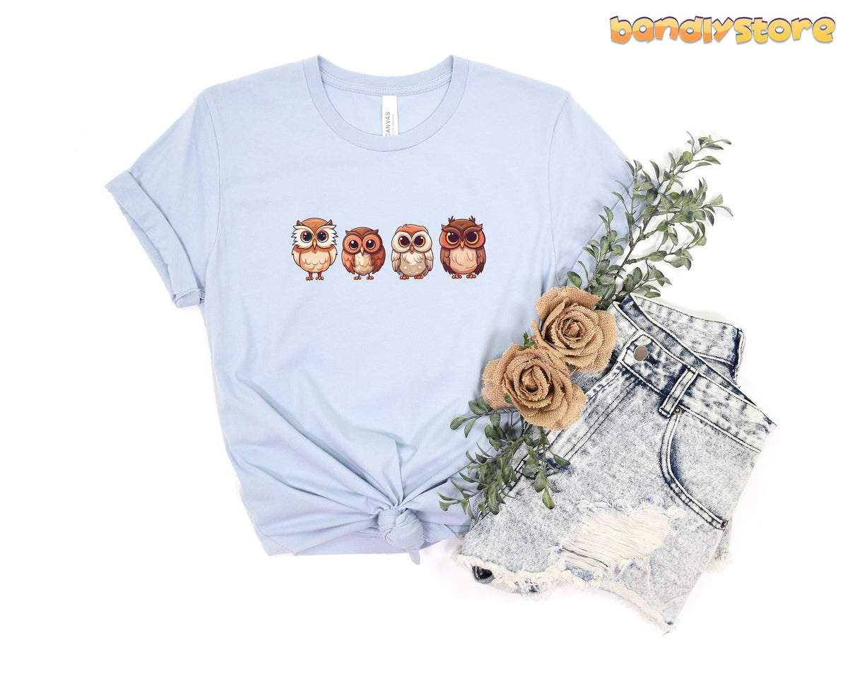 Cute Owl T-Shirt in light blue, flat-laid with four owls beside ripped denim shorts, leaves and burlap roses.