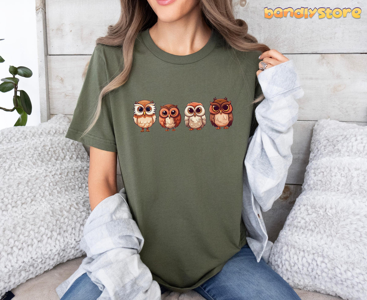 Cute Owl T-Shirt in military green with four owls, front view worn seated amid white pillows and wooden wall.
