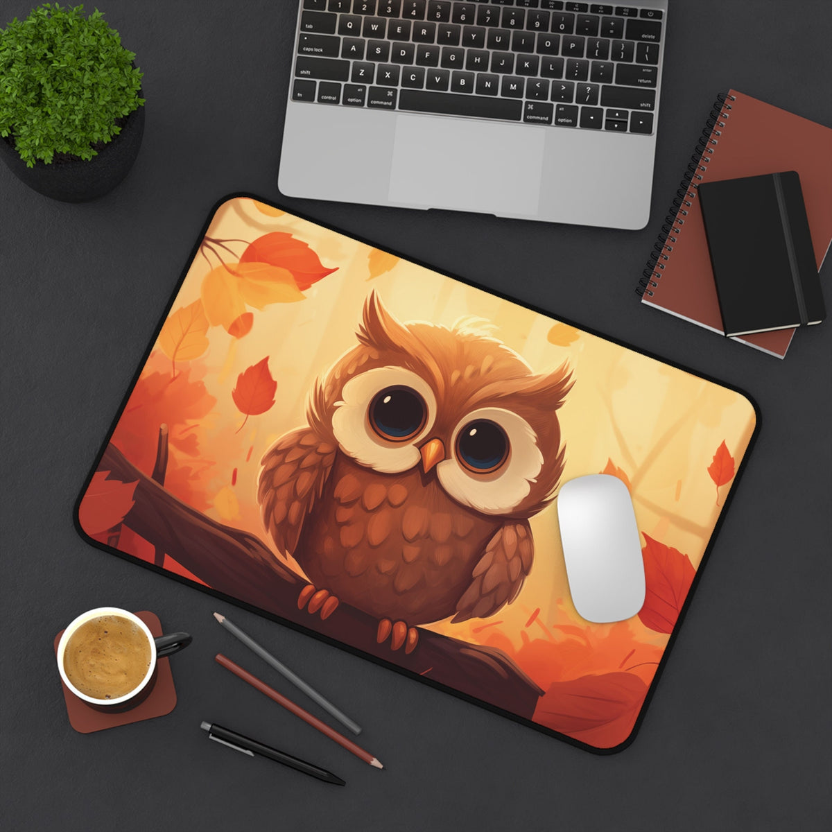 Cute Owl Desk Mat 12 × 18 inches shown from above on a dark desk next to a laptop, plant, notebooks, coffee, pens and mouse.