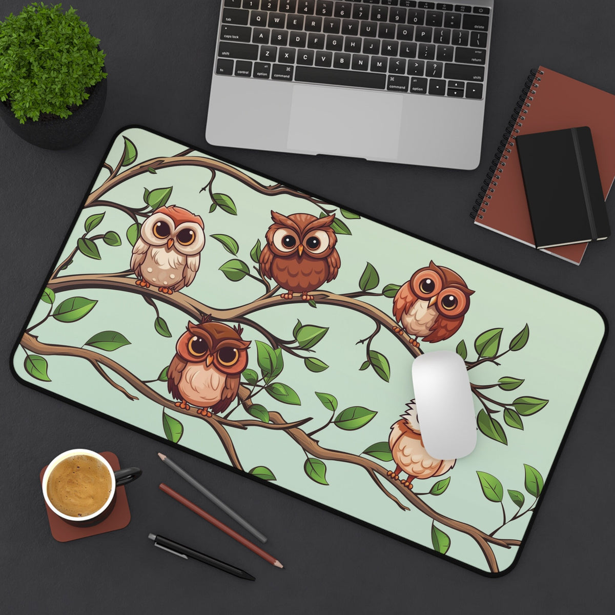 Cute Owls Desk Mat 12 × 22 inches in overhead view on a desk with laptop, plant, coffee, pens, notebooks and mouse.