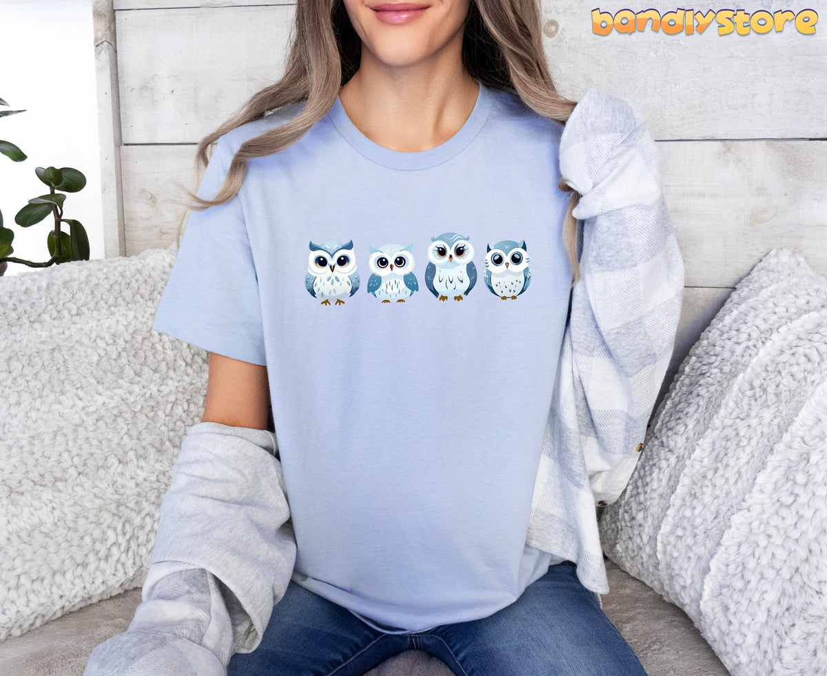 Cute Snow Owl T-Shirt in light blue on a seated model amid couch pillows and a plant.
