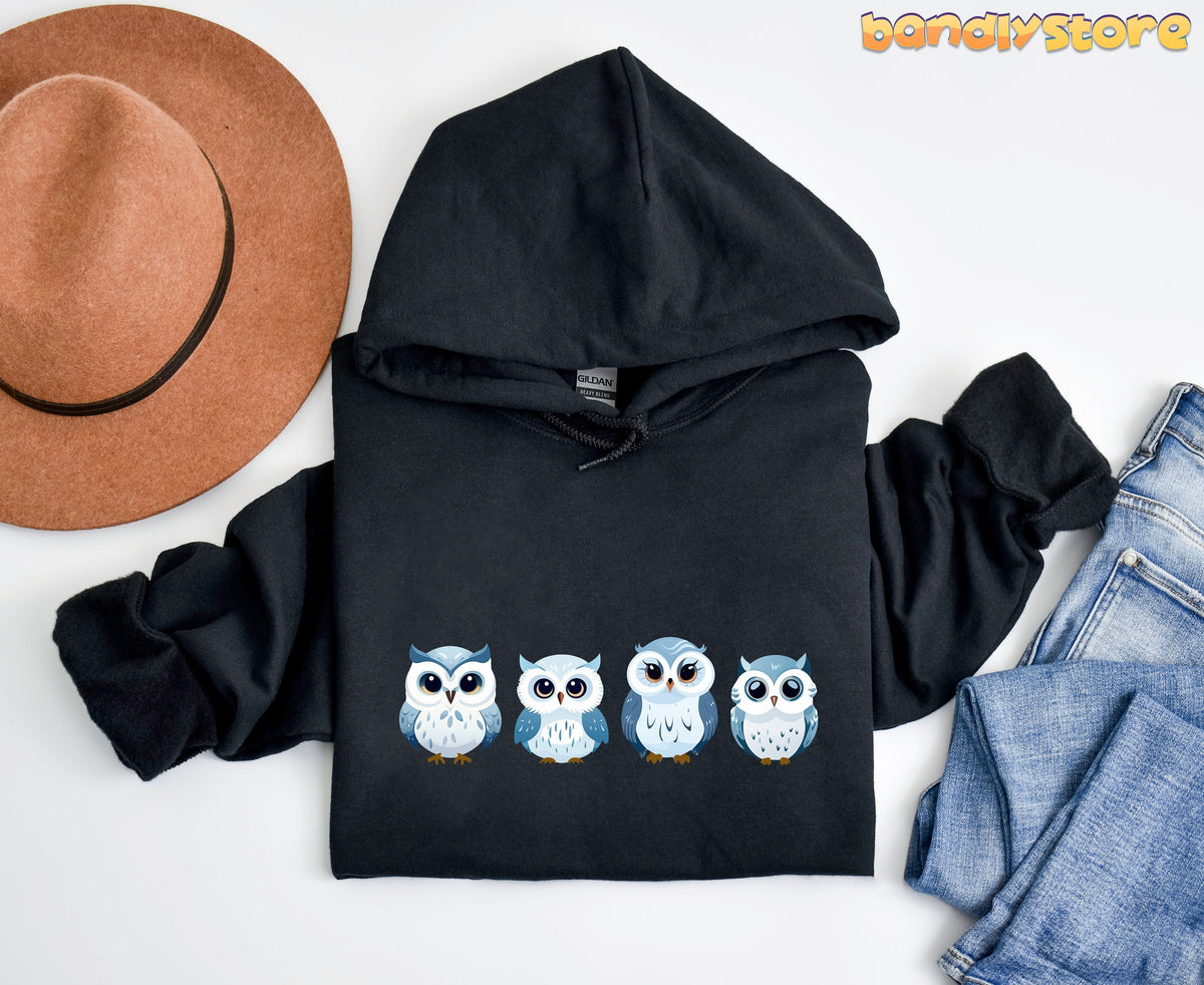 Cute Snow Owl Hoodie in black laid flat from above beside a brown hat and blue jeans.
