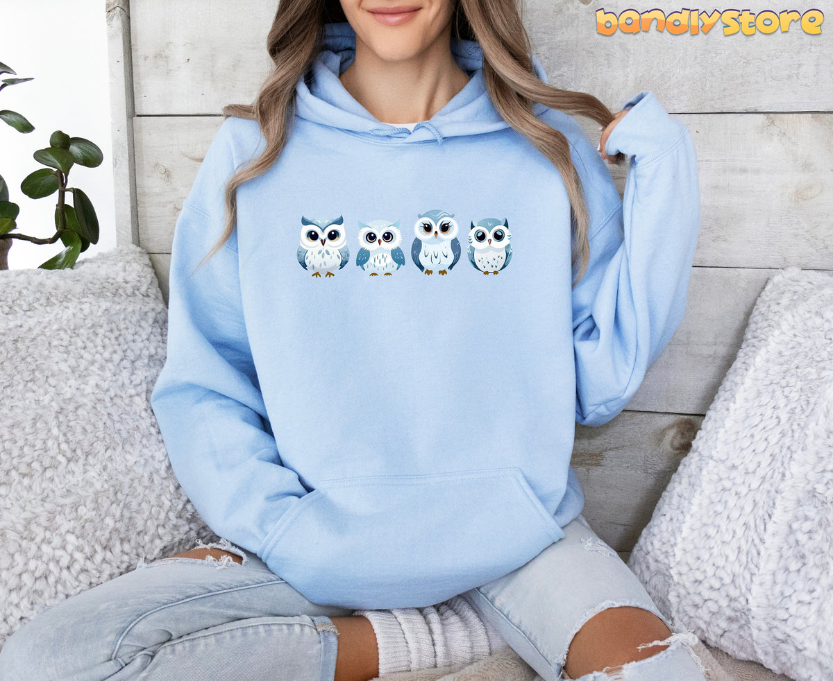 Cute Snow Owl Hoodie in light blue on seated person against wooden wall with pillows and plant.