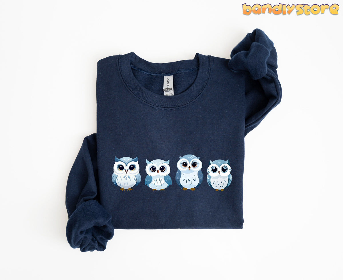 Cute Snow Owl Sweatshirt on folded navy garment, top-down view with four cartoon owls across the chest.