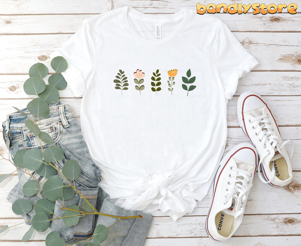 Cute Wildflowers T-Shirt in white flat on wood beside jeans, greenery and sneakers.