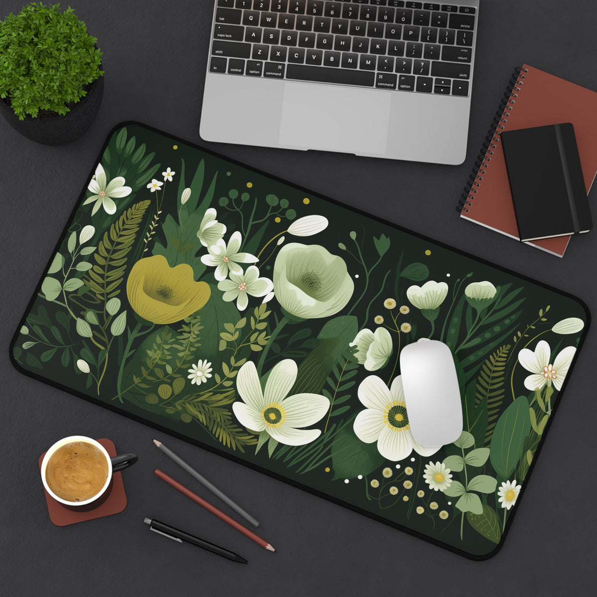 Dark Floral Desk Mat 12 × 22 inches on a desk from above next to laptop, plant, mouse, coffee, pencils and notebooks.