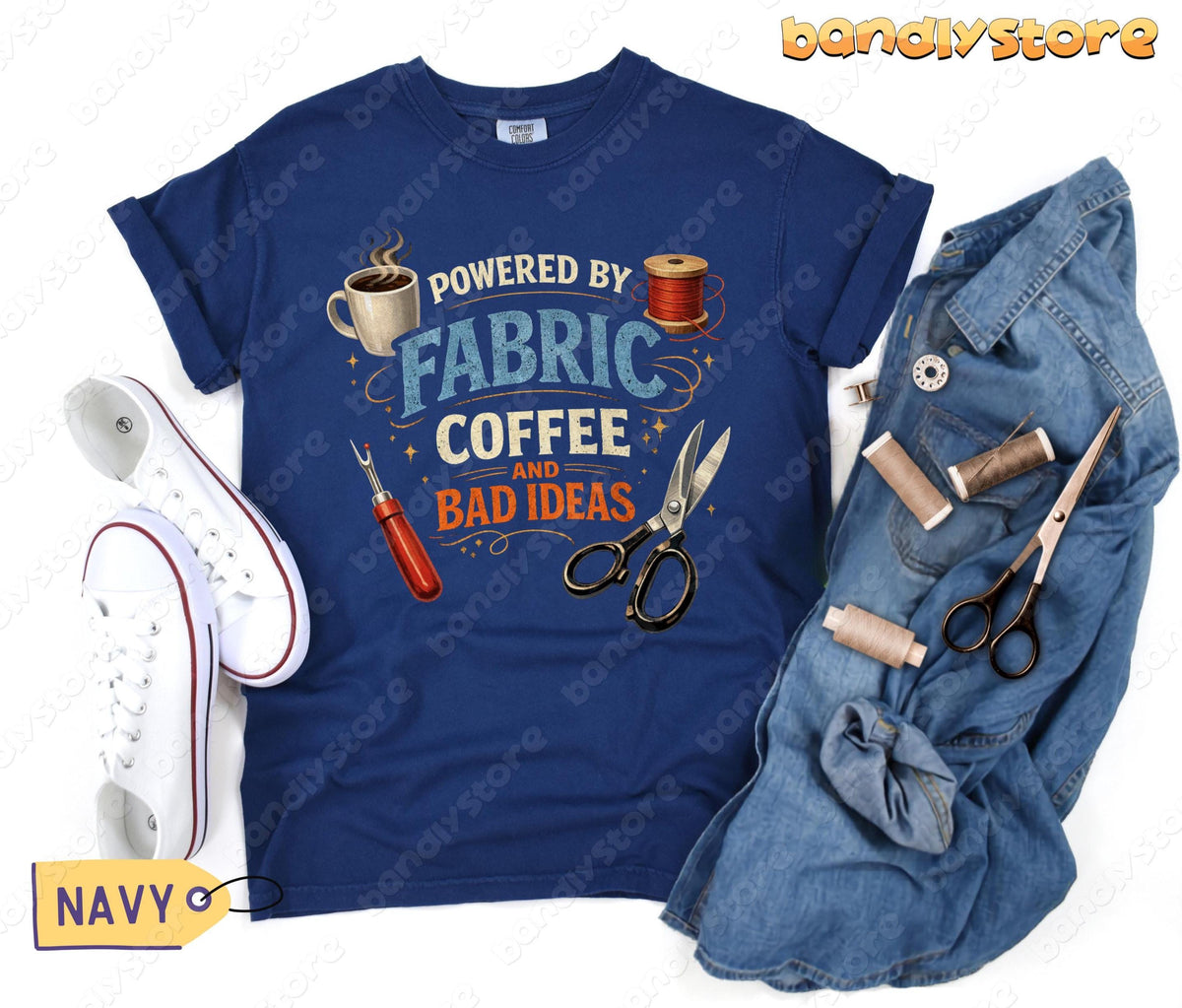 Powered By Fabric, Coffee And Bad Ideas T-Shirt in navy laid flat beside white sneakers and denim with sewing tools.