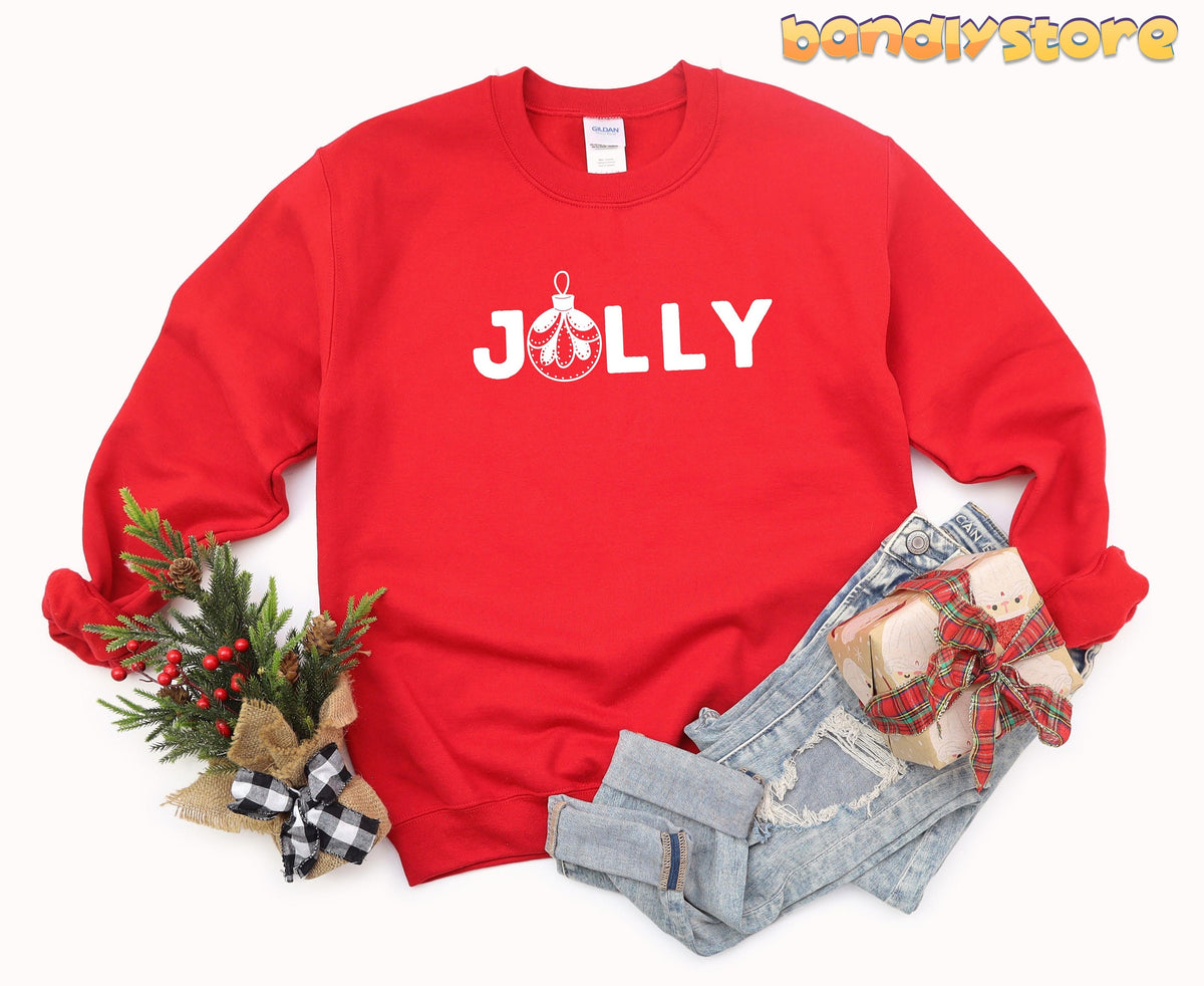 Feeling Jolly Christmas Sweatshirt in red, flat lay with pine greenery, jeans and wrapped gift.