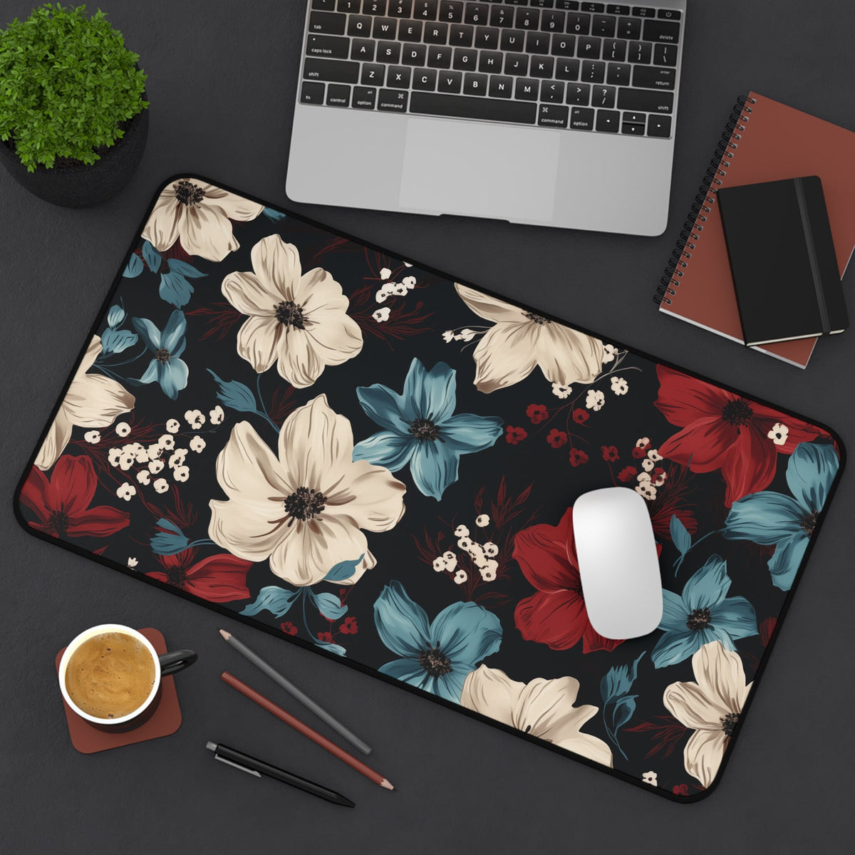 Dark Floral Desk Mat in 12 × 22 inches on a desk from above, with laptop, mouse, plant, notebooks, coffee and pens.